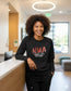 Smiling nurse wearing black Nurses With Attitude sweatshirt and black FIGS scrub joggers in a modern clinic.