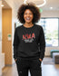 Smiling nurse wearing black Nurses With Attitude sweatshirt and black FIGS scrub joggers in a modern clinic